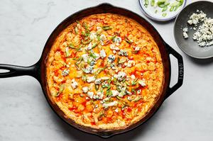homemade buffalo chicken dip in a cast iron skillet fresh out of the oven topped with blue cheese crumbles and green onions