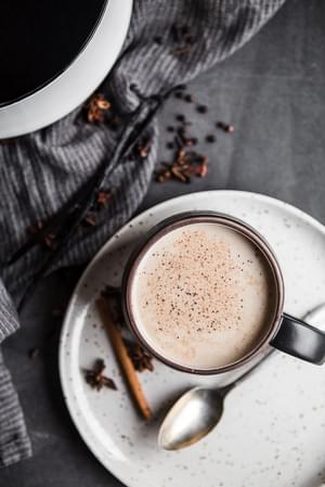 A mug of homemade chai tea with a spoon and a linen on a plate.