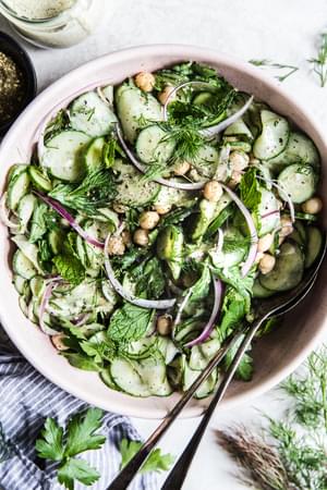 cucumber salad with chickpeas, onion, parsley, mint, dill and a yogurt dressing in a bowl with serving spoons