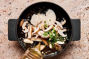chicken stock being added to a pot with soy sauce, scallions, mushrooms, chicken, ginger and garlic