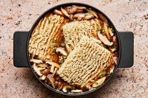 ramen noodles being added to a pot of chicken stock, soy sauce, spices and mushrooms