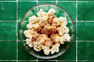 cauliflower being tossed with taco seasoning, olive oil and lime juice in a glass bowl