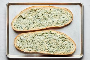a loaf of french bread sliced in half topped with a butter parmesan spread on a baking sheet to make french bread pizza