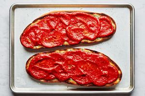 french bread sliced in half topped with butter, spices and pizza sauce on a baking sheet to make french bread pizza