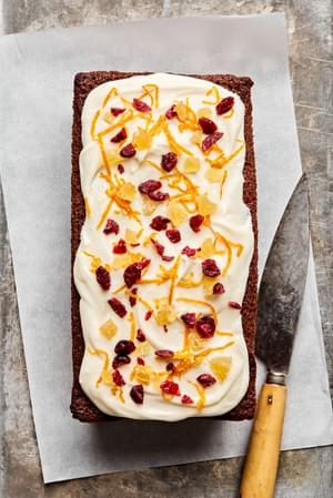 gingerbread loaf topped with cream cheese frosting, candied ginger, orange zest and dried cranberries
