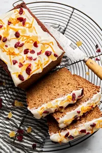 sliced gingerbread loaf topped with cream cheese frosting, candied ginger, orange zest and dried cranberries