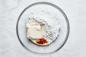 powdered sugar, cream cheese, vanilla, salt, and heavy cream being mixed in a bowl to make cream cheese frosting