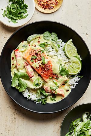 homemade green curry salmon served on top of white rice garnished with green onions, cilantro and red pepper flakes