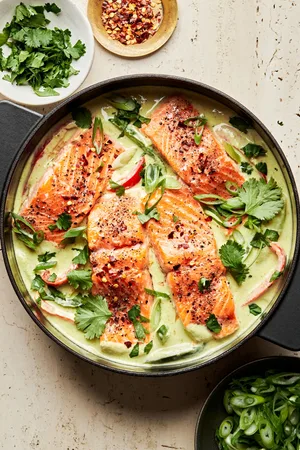 homemade green curry salmon in a large pot made with coconut milk, lime juice, ginger, fish sauce, peppers and onions