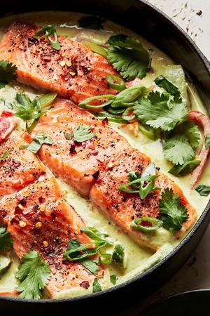 homemade green curry salmon in a large pot made with coconut milk, lime juice, ginger, fish sauce, peppers and onions