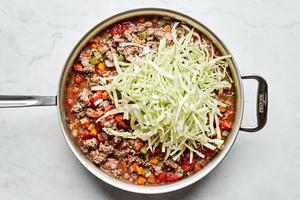 cabbage being added to a skillet of healthy shepherd's pie filling made with beef, onion, carrots, celery, and garlic