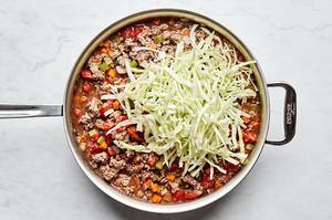cabbage being added to a skillet of healthy shepherd's pie filling made with beef, onion, carrots, celery, and garlic