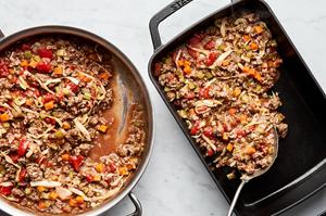 healthy shepherd's pie filling with ground beef, onion, carrots and cabbage being scooped from a skillet into a baking dish