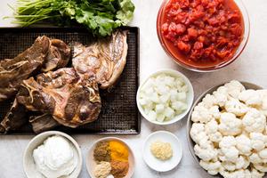 Ingredients laid out for lamb curry cilantro, canned tomatoes, cauliflower, spices, garlic, onion and yogurt.