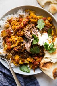A bowl of Indian Style Lamb Curry With Cauliflower over white rice and served with yogurt and cilantro and naan