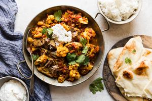 Indian Style Lamb Curry With Cauliflower in a serving side next to rice and naan.