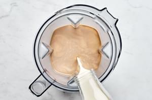 heavy creamed being poured in a blender with condensed milk, whiskey, chocolate, vanilla, instant coffee and coconut cream
