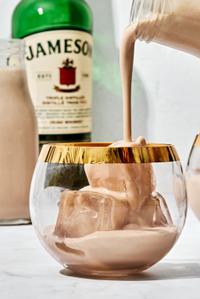 homemade Irish cream liqueur being poured into a cocktail glass over ice