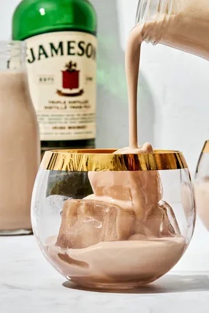 homemade Irish cream liqueur being poured into a cocktail glass over ice