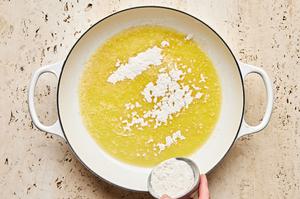 flour being sprinkled into a pan of melted butter