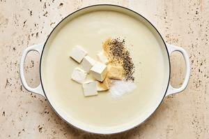 salt, garlic, pepper and cream cheese being added to a skillet with a rue made of butter and flour