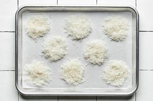 tablespoon sized piles of grated parmesan cheese on a parchment lined baking sheet