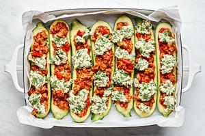 zucchini boats filled with ground chicken, marinara and a ricotta filling in a parchment lined baking dish