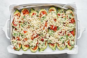 lasagna stuffed zucchini goats in a parchment lined baking dish sprinkled with mozzarella cheese