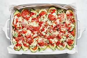 lasagna stuffed zucchini boats in a parchment lined baking dish sprinkled with mozzarella and topped with extra marinara