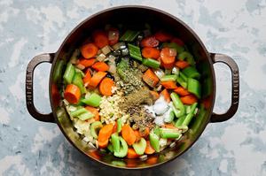 spices being added to a pot with carrots, celery and onion that have been cooked in olive oil