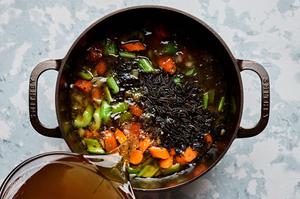 stock and wild rice being added to a pot with carrots, onion, celery and spices