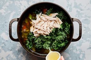 shredded turkey and kale being added to a pot of soup
