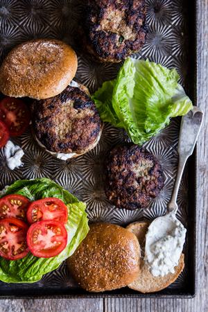 Mediterranean Turkey Burgers on a baking sheet with whole wheat buns, lettuce tomatoes and tzatziki sauce on a spoon