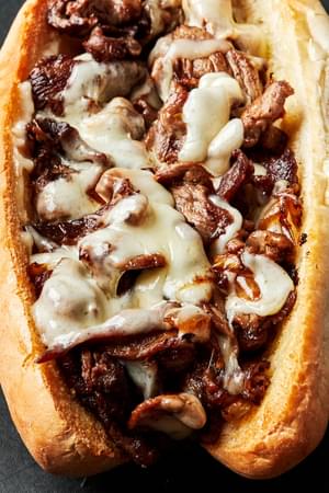 a close up of a homemade Philly cheese steak sandwich on a hoagie roll topped with melted provolone cheese