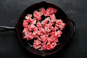 thinly sliced beef seasoned with salt cooking in vegetable oil in a cast iron skillet to be used for Philly cheesesteaks