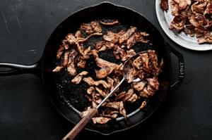 cooked beef being spooned out of a cast iron skillet into a bowl