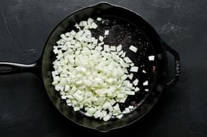 chopped onions being cooked in a cast iron skillet to be added with beef for philly cheesesteaks