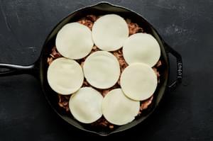 cooked beef in a cast iron skillet with sliced provolone on top of it ready to be melted in the oven for Philly cheesesteaks