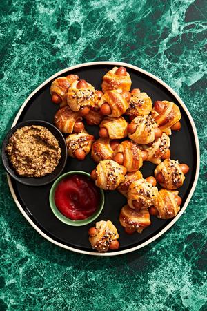 pigs in a blanket topped with everything bagel seasoning on a serving platter served with ground mustard and ketchup