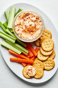 homemade pimento cheese in a bowl on a serving platter with celery, carrots and ritz crackers
