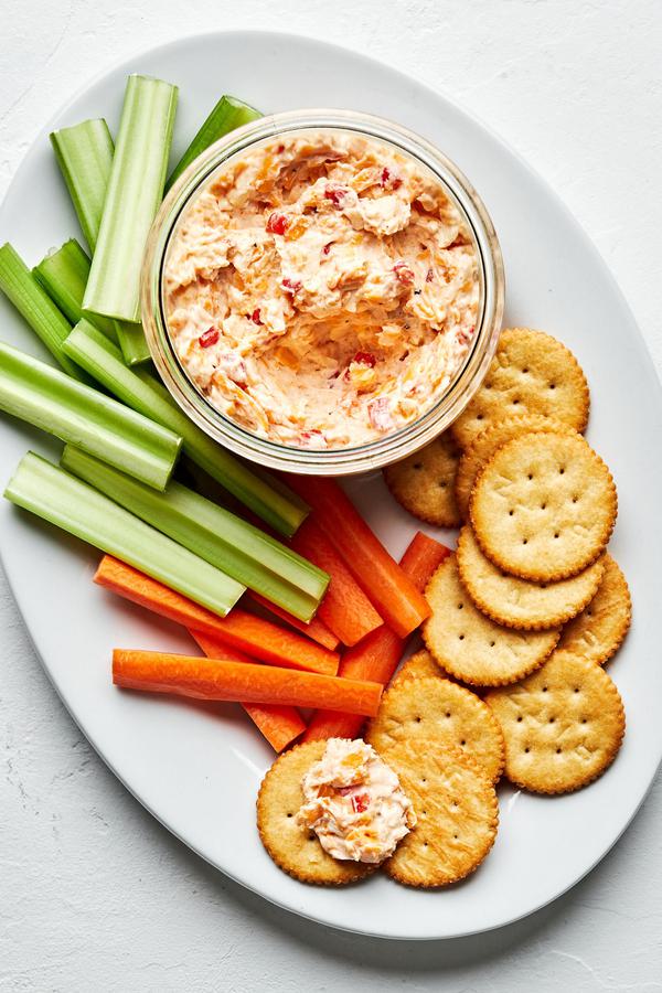 homemade pimento cheese in a bowl on a serving platter with celery, carrots and ritz crackers