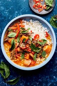 red curry beef with sweet potatoes, onion and red bell peppers served over rice topped with cilantro and basil
