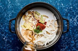 coconut milk, beef stock, red curry paste, lime zest, lime juice, onion, garlic, lemongrass, and ginger being added to a pot