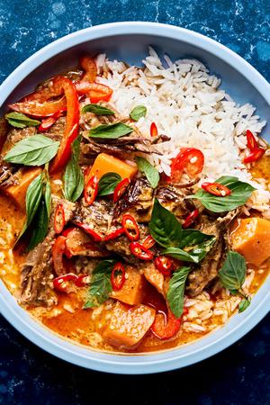 red curry beef with sweet potatoes, onion and red bell peppers served over rice topped with cilantro and basil