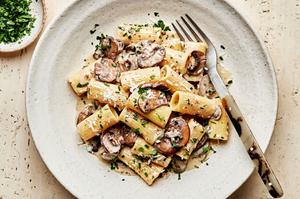 homemade rigatoni with mushroom sauce in a pasta bowl with a fork made with cream, parmesan, chives, parsley and wine