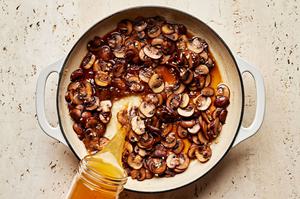 chicken stock and wine being added to a pot with mushrooms and garlic that were cooked in butter and olive oil