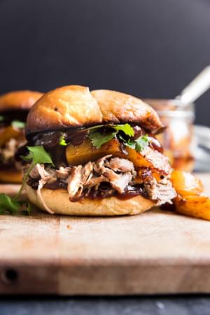 slow cooker pork sandwich with cilantro pineapples, onions and bbq sauce on a bun on a butting board.