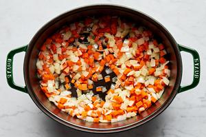carrots and onions being cooked in a large soup pot with melted butter to use in tomato bisque