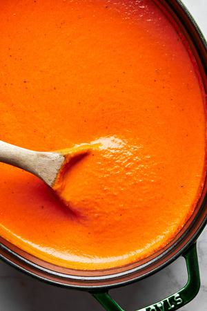 homemade tomato bisque made with tomatoes, carrots, onion, spices, basil and cream in a pot being stirred with a wooden spoon
