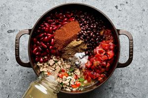 spices, beans and chicken stock being added to a pot with ground turkey and vegetables